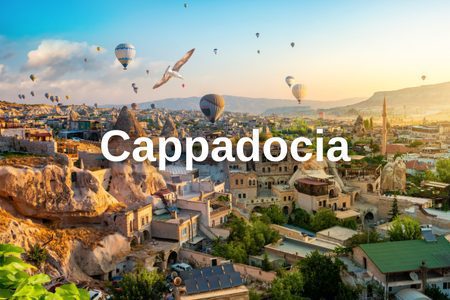 Hot air balloons flying over the rock formations and historic buildings of Cappadocia during sunrise.